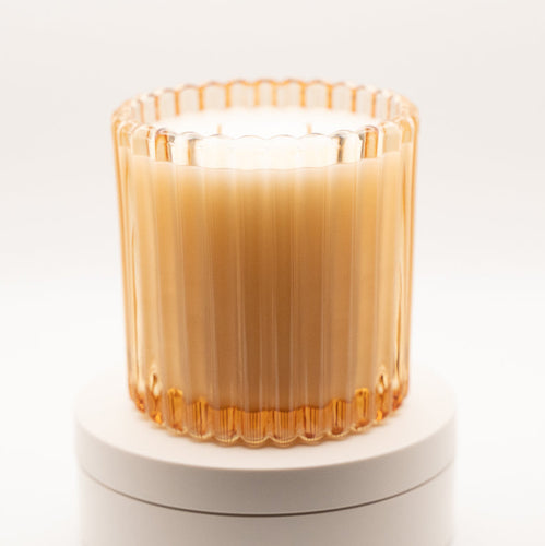 Candle in a ribbed glass container on a white base with a white background